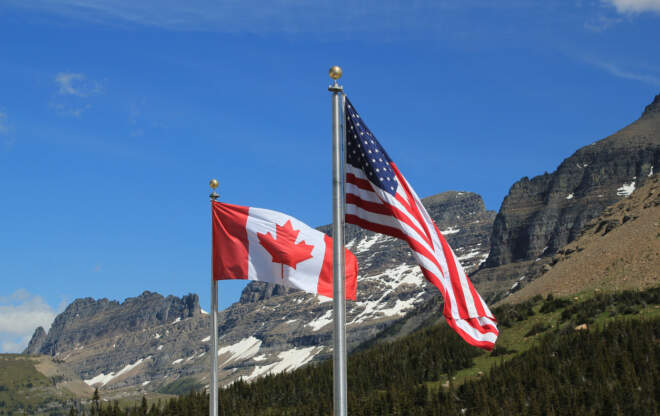 Canada and US flags fly near a bridge.