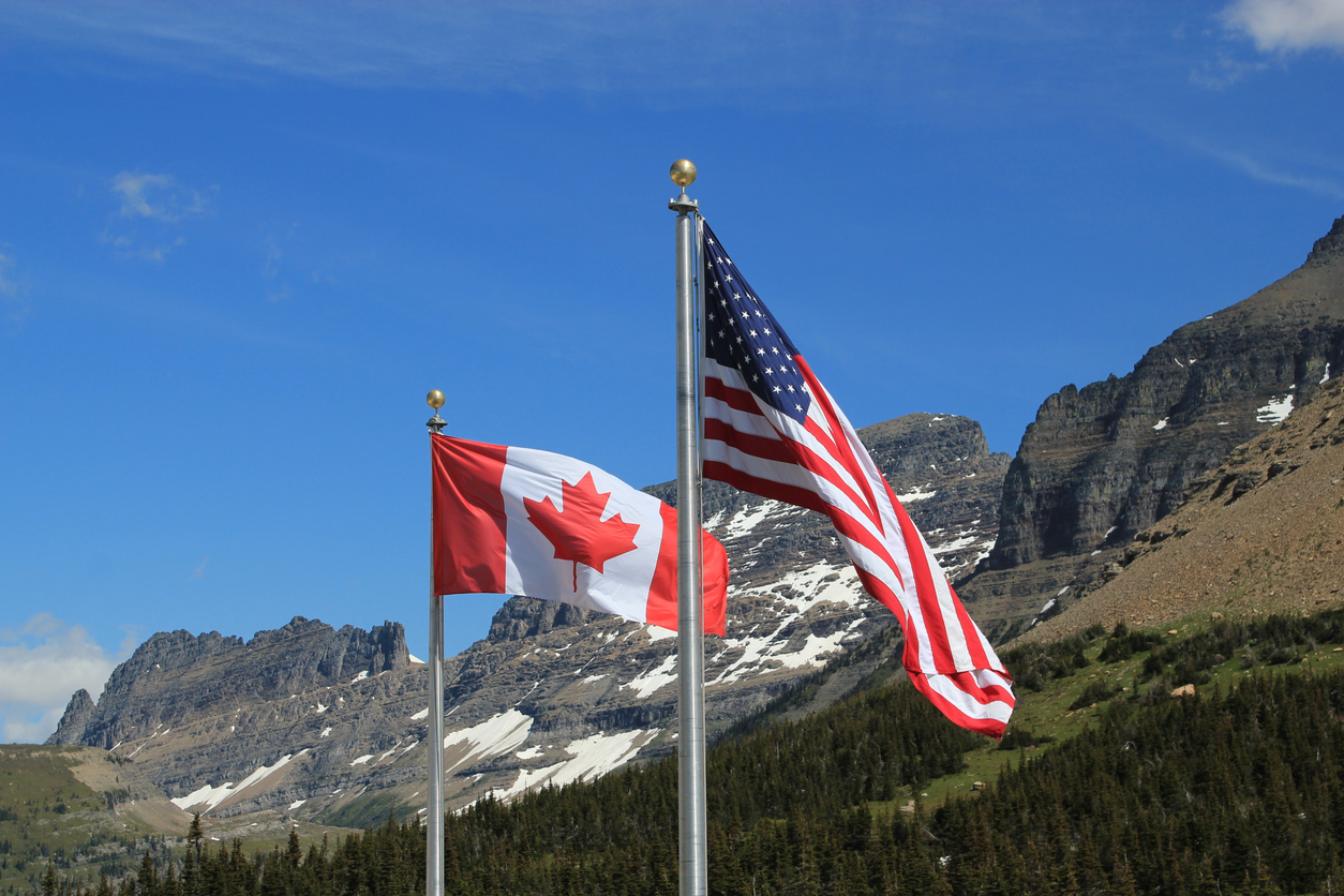 Canada and US flags fly near a bridge.