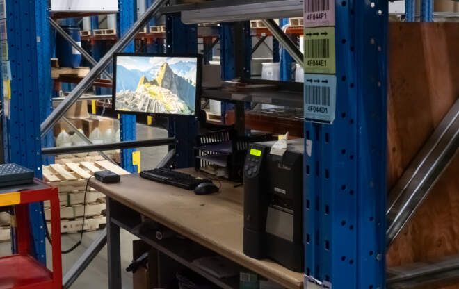 A computer screen in a warehouse depicts an environment with inventory control software.