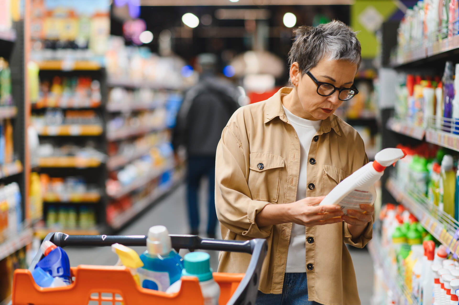 Senior woman shopping household chemicals in supermarket aisle